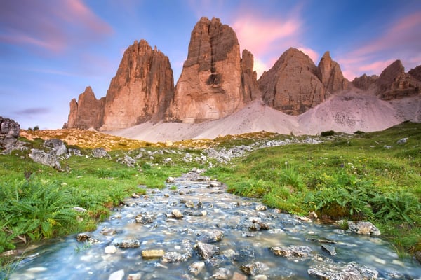 Blick auf die Drei Zinnen mit felsigem Gebirge und klarem Bach in grüner Alpennatur