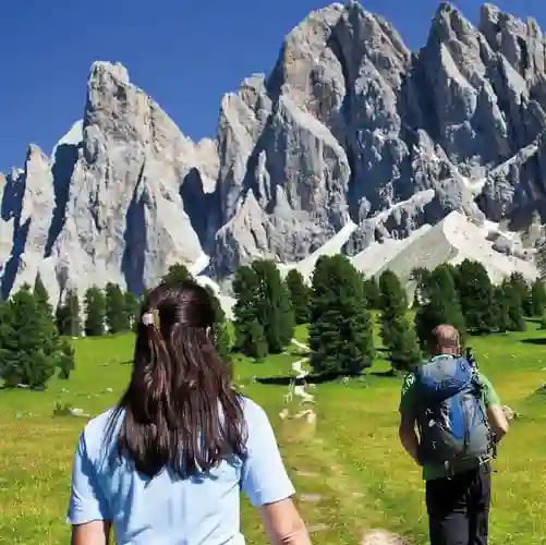Wanderer auf Almweg mit Blick auf steile Dolomiten Gipfel und grüne Wiesen
