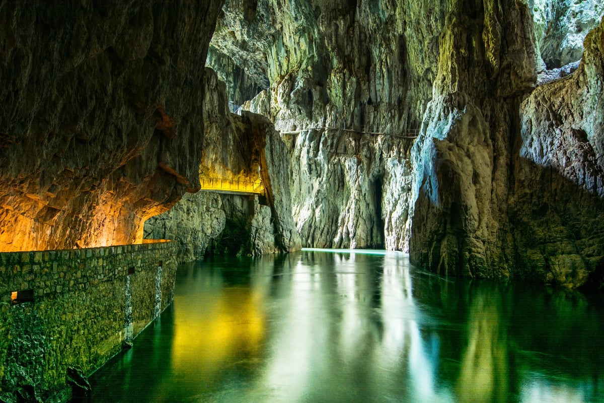 Beleuchtete Tropfsteinhöhle mit unterirdischem Fluss und Felswänden
