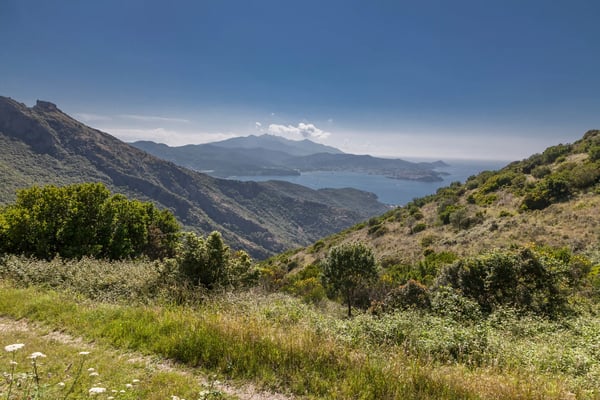 Weitblick über grüne Hügel auf das Meer und eine Bucht in der Ferne