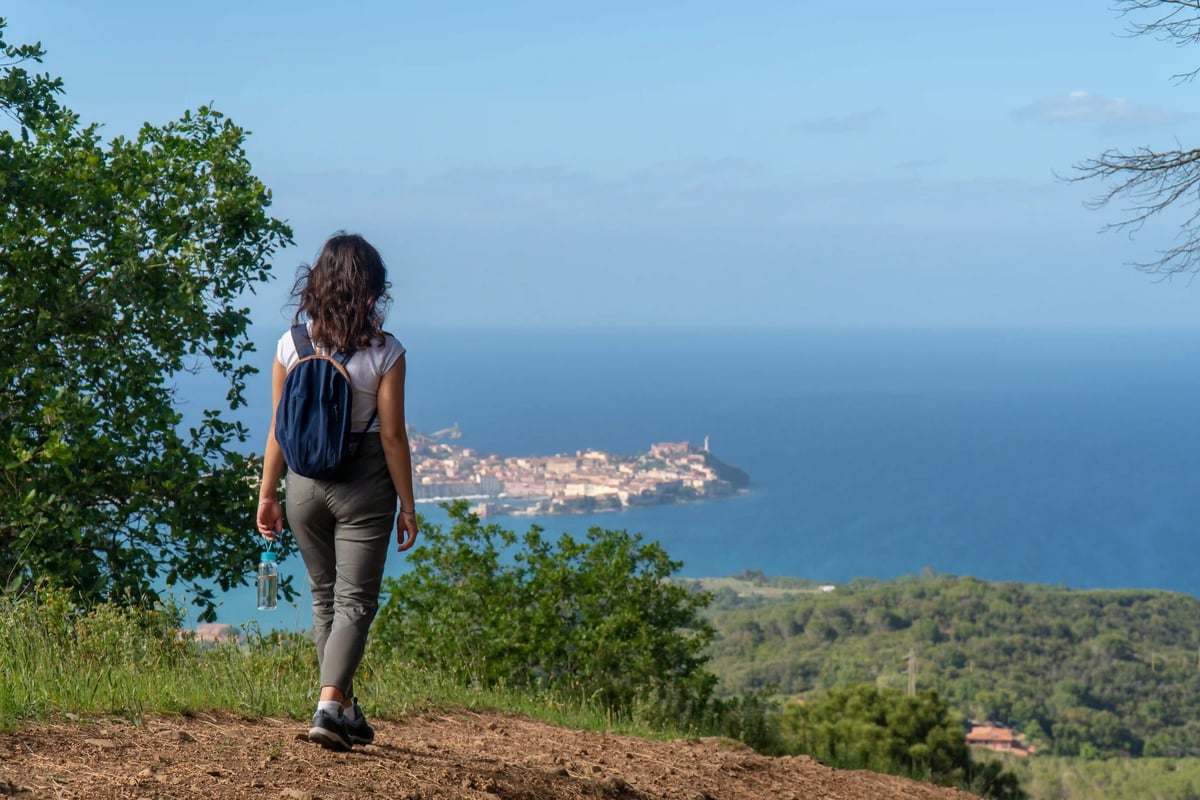Randonneuse avec sac à dos face à la côte et une ville en bord de mer