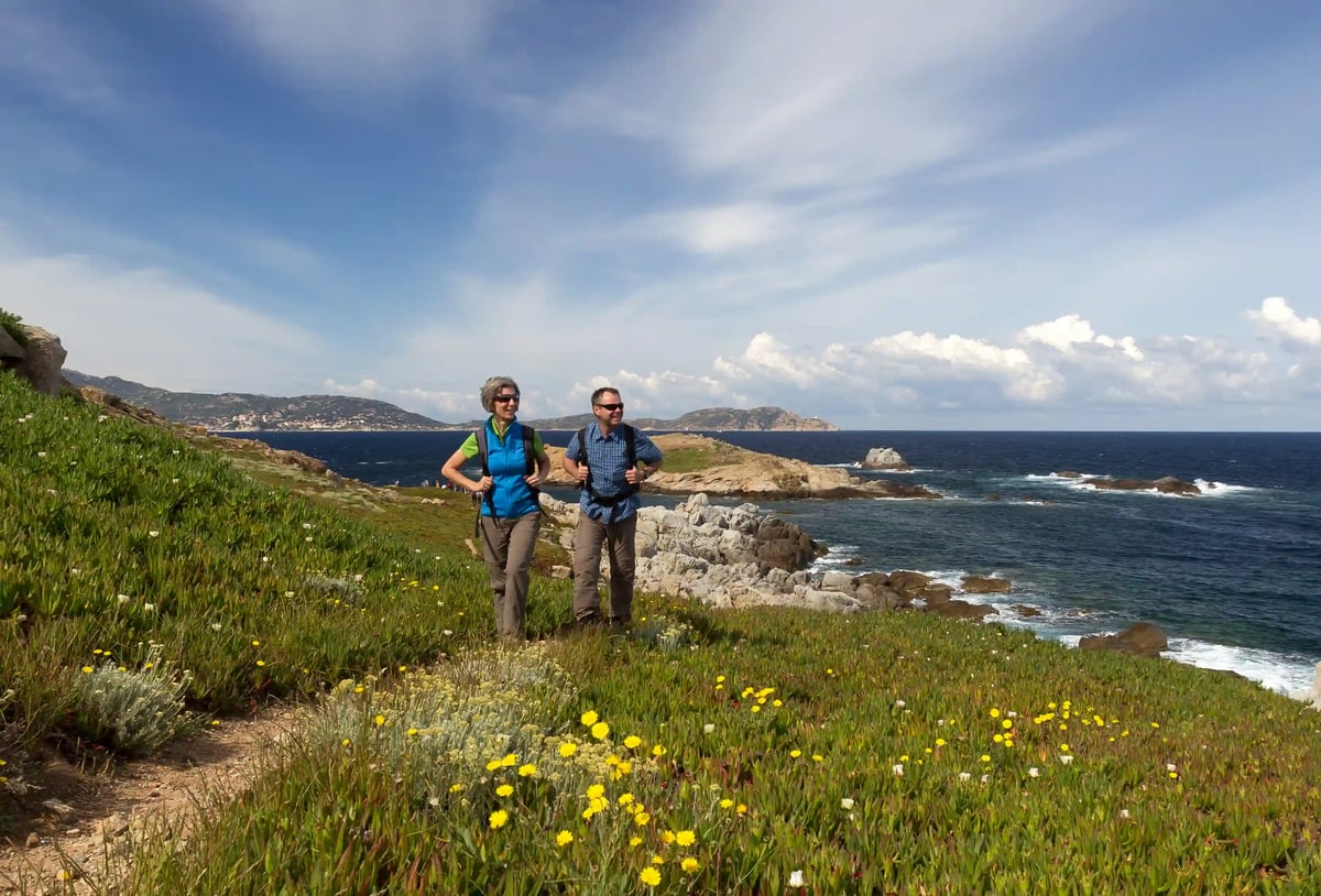 Deux randonneurs sur un sentier côtier en Corse avec vue sur la mer et paysage rocheux