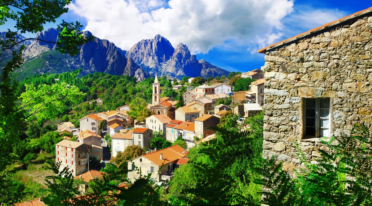 Village de montagne traditionnel en Corse avec maisons en pierre et massif rocheux en arrière-plan
