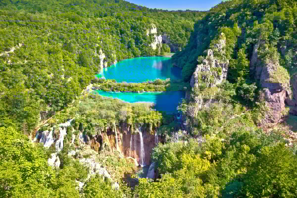 Blick auf türkisfarbene Seen und Wasserfälle im Nationalpark Krka, umgeben von dichtem grünem Wald und Felsen