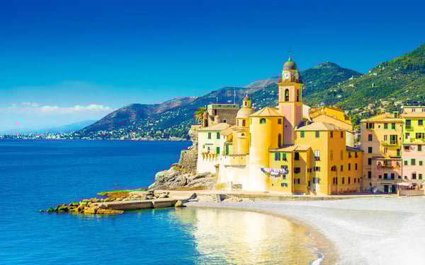 Bunte Häuser von Camogli direkt am Strand mit Kirche, Meer und Bergen im Hintergrund