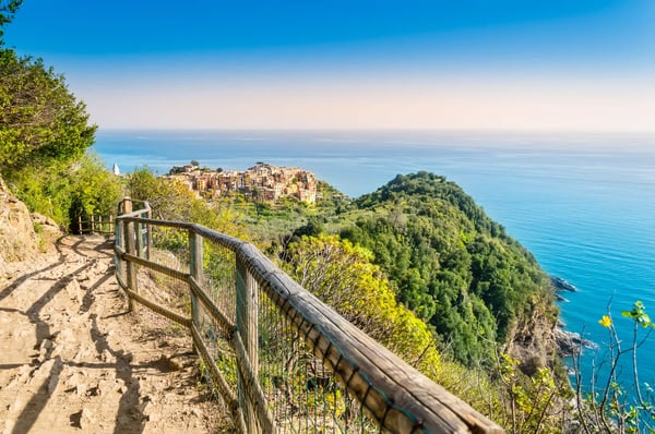 Schmaler Wanderweg mit Holzgeländer und Blick auf Corniglia hoch über dem Meer in den Cinque Terre