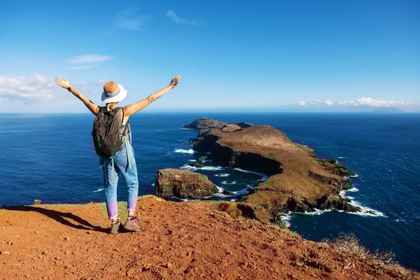 Frau mit Rucksack steht an einem Aussichtspunkt mit Blick auf Meer und felsige Halbinsel