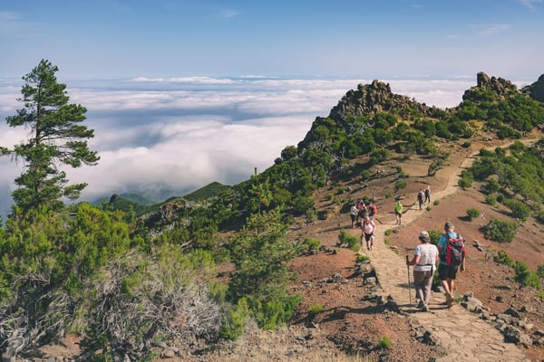 Wandergruppe auf schmalem Bergpfad oberhalb der Wolken mit Blick auf Gipfel