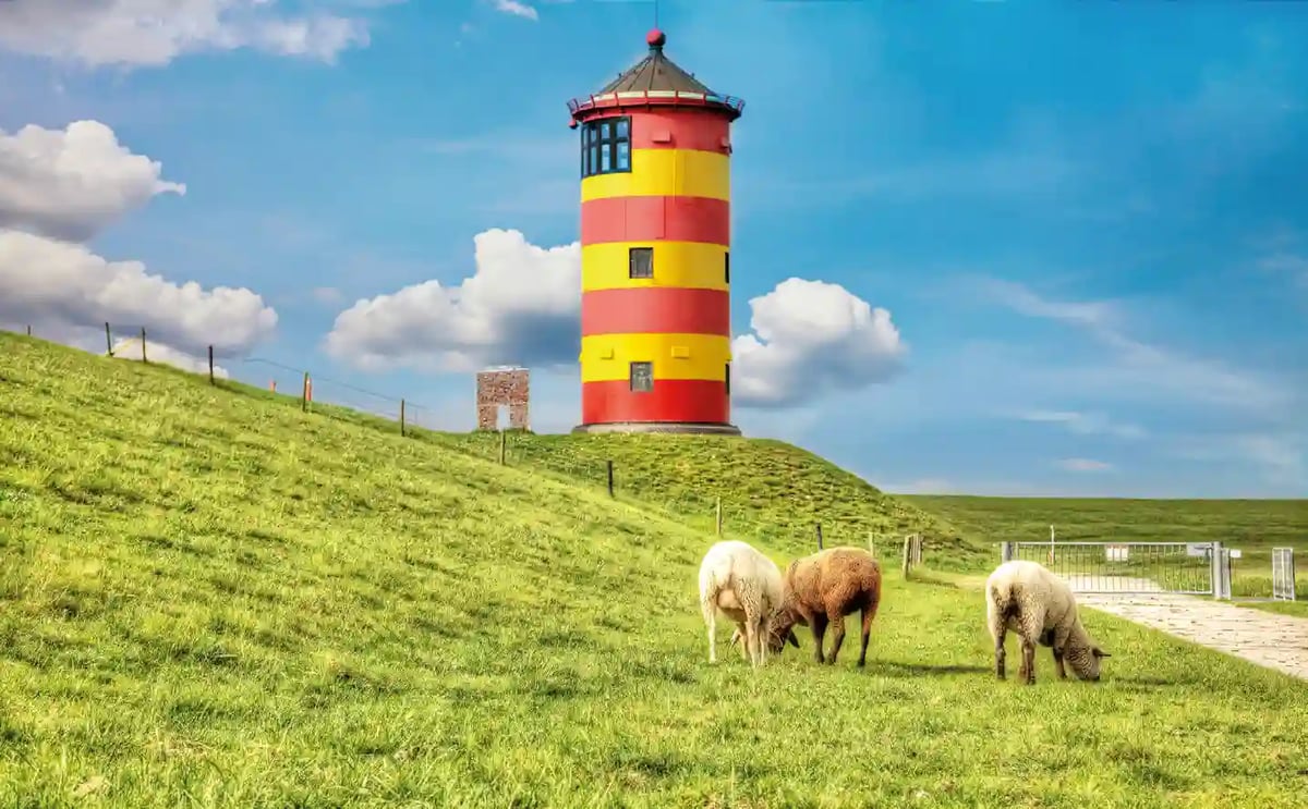 Der rot-gelb gestreifte Pilsumer Leuchtturm in weiter Marschlandschaft unter blauem Himmel