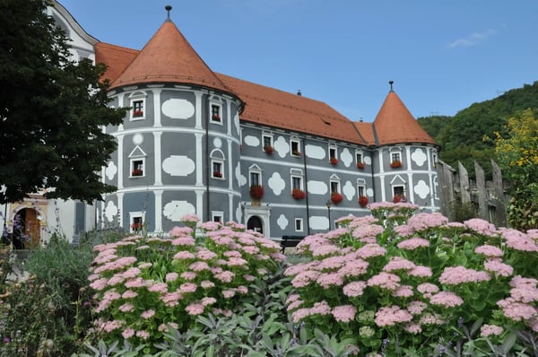 Kloster Olimje mit grauer Fassade, roten Dächern und blühendem Garten
