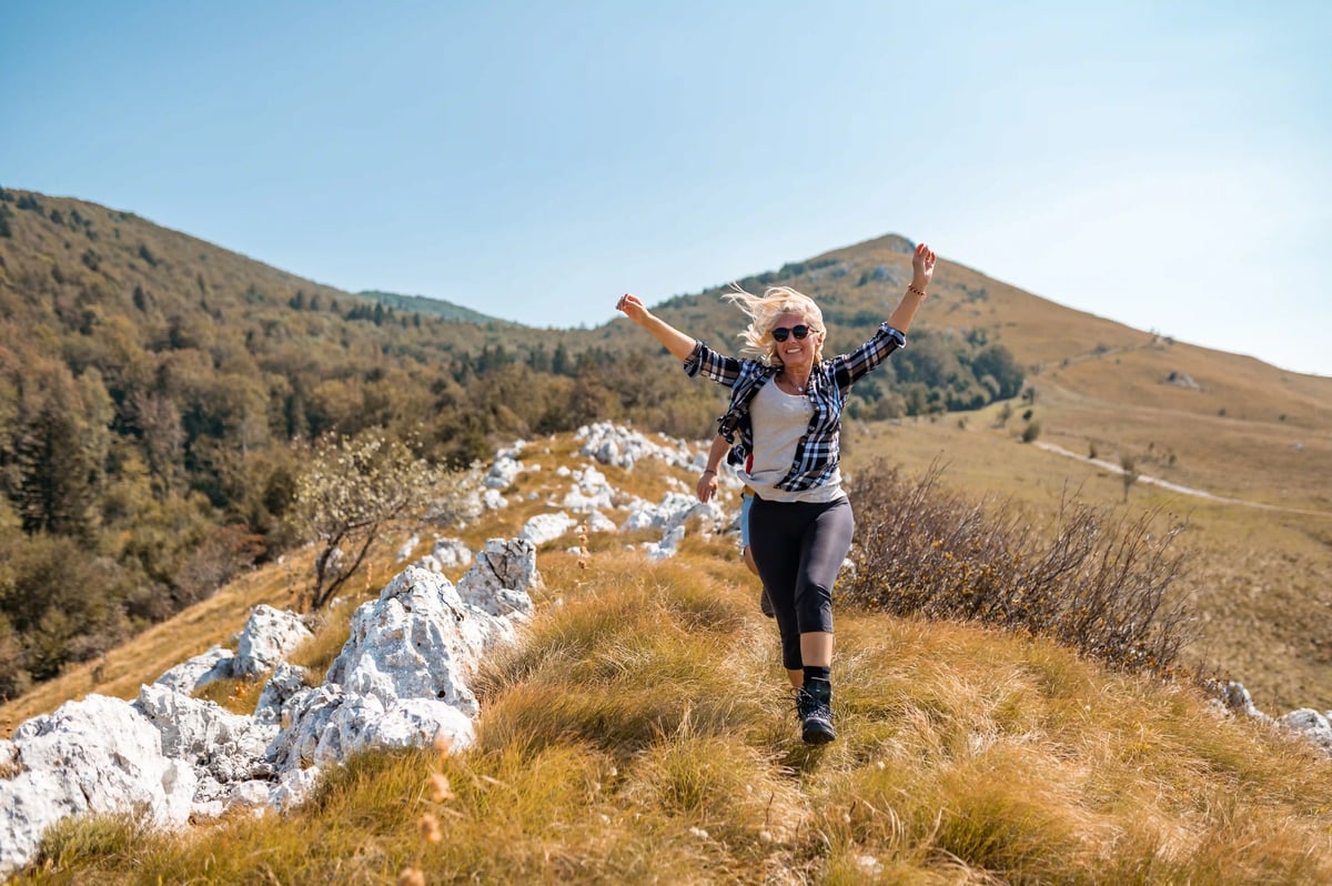 Wanderin auf Bergpfad in slowenischer Hügellandschaft mit erhobenen Armen