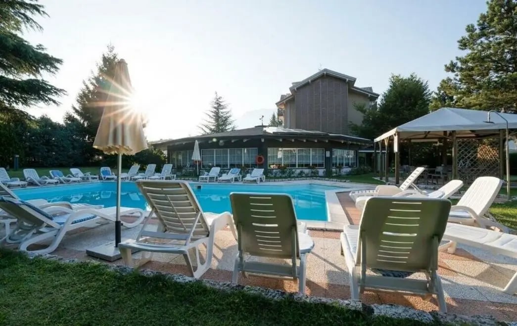 Hôtel avec piscine extérieure, chaises longues et parasols dans un cadre verdoyant et calme