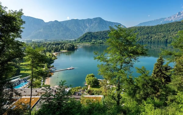 Blick auf den See bei Levico Terme mit grünen Wäldern, Bergen und ruhiger Uferlandschaft