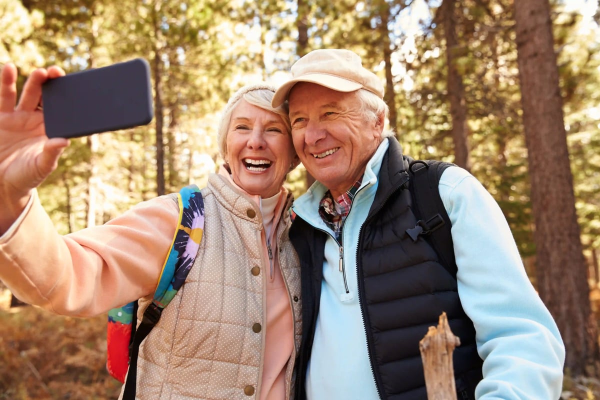Couple senior souriant prenant un selfie lors d’une randonnée dans une forêt automnale