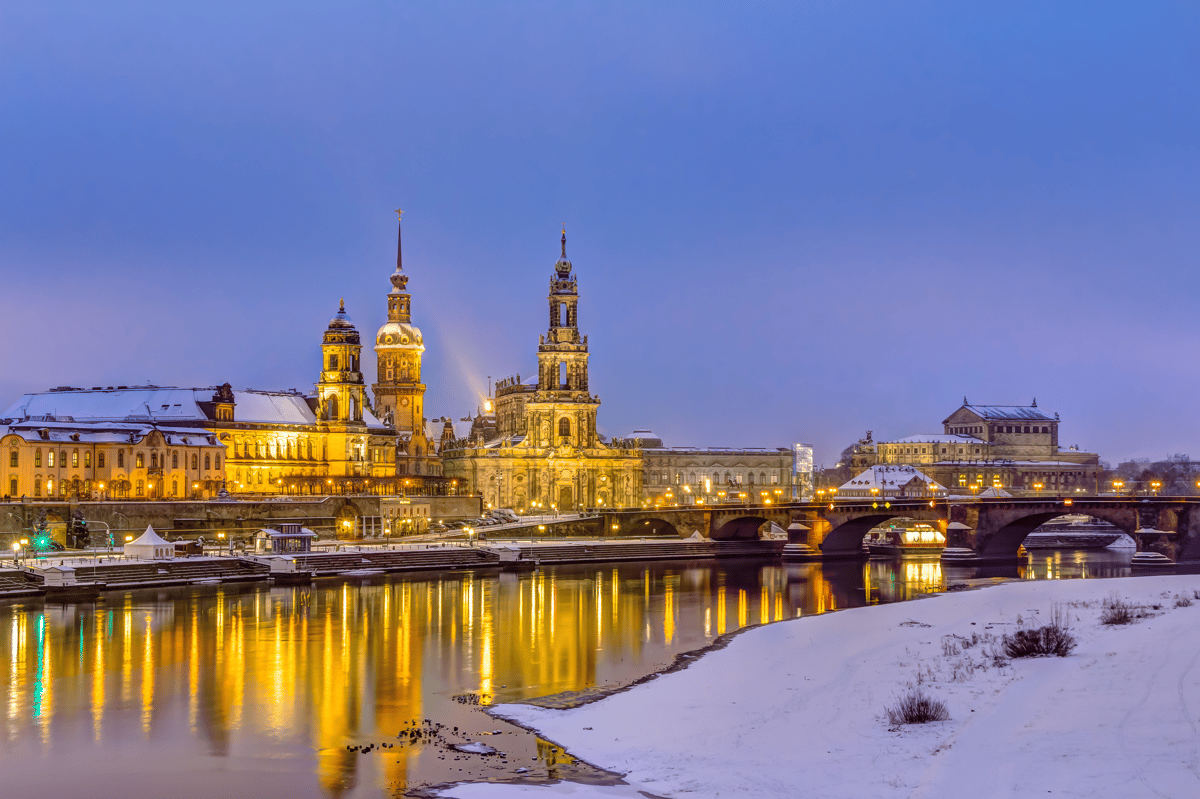 Verschneite Altstadt von Dresden mit Frauenkirche und beleuchteter Stadtsilhouette an der Elbe.