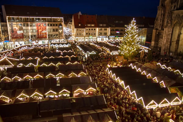 Belebter Weihnachtsmarkt in Ulm bei Nacht mit beleuchteten Buden und Baum