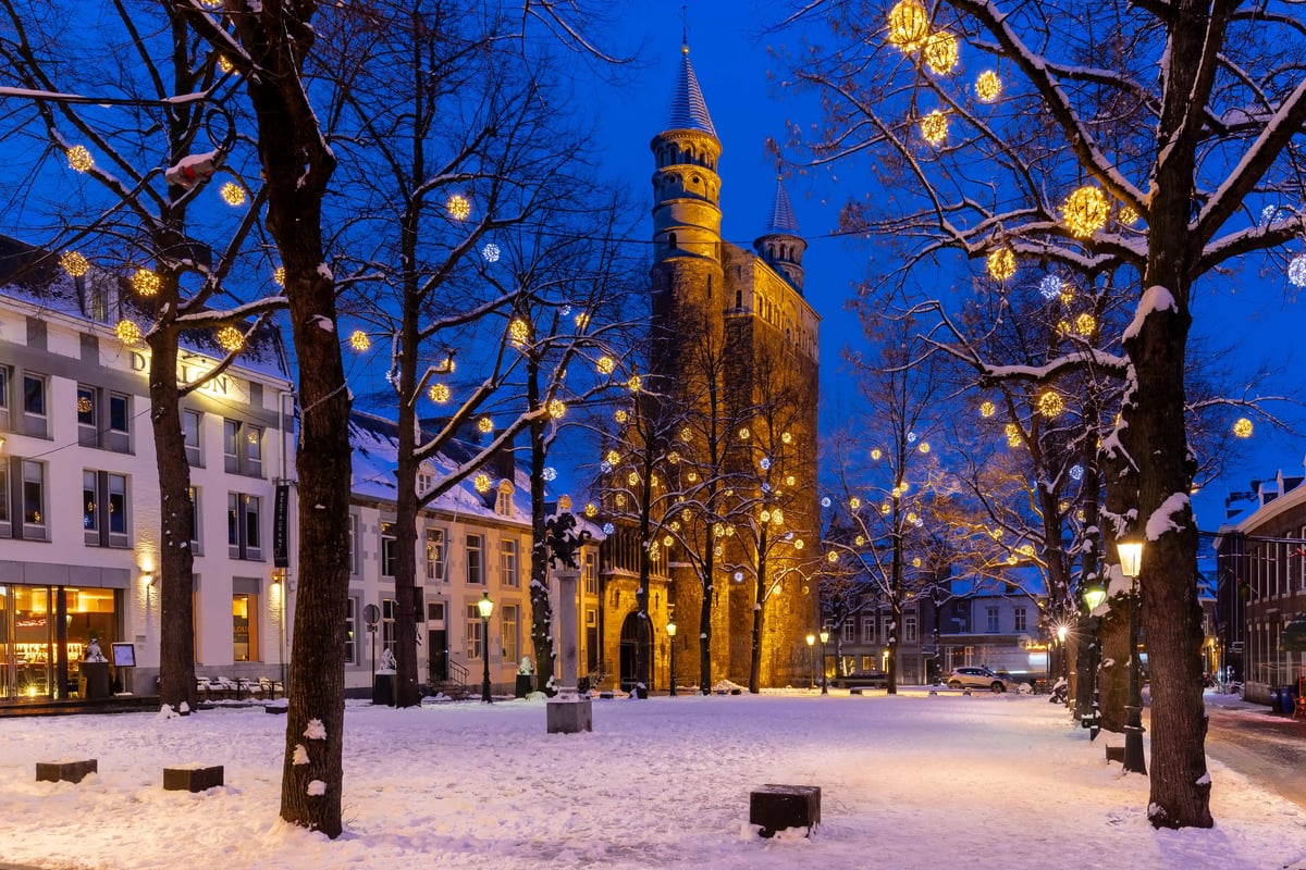 Verschneiter Platz in Maastricht mit beleuchteter Kirche und festlich geschmückten Bäumen