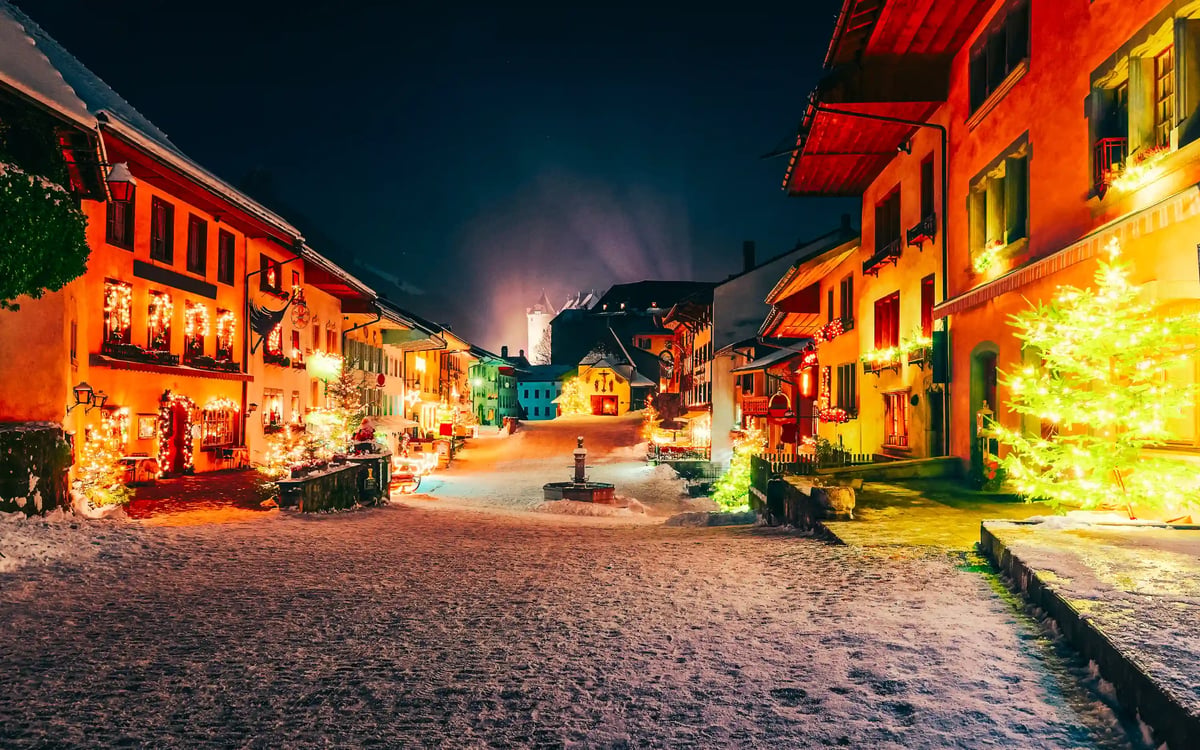 Verschneite Strasse in einem Dorf bei Nacht mit festlich beleuchteten Haeusern und Dekoration