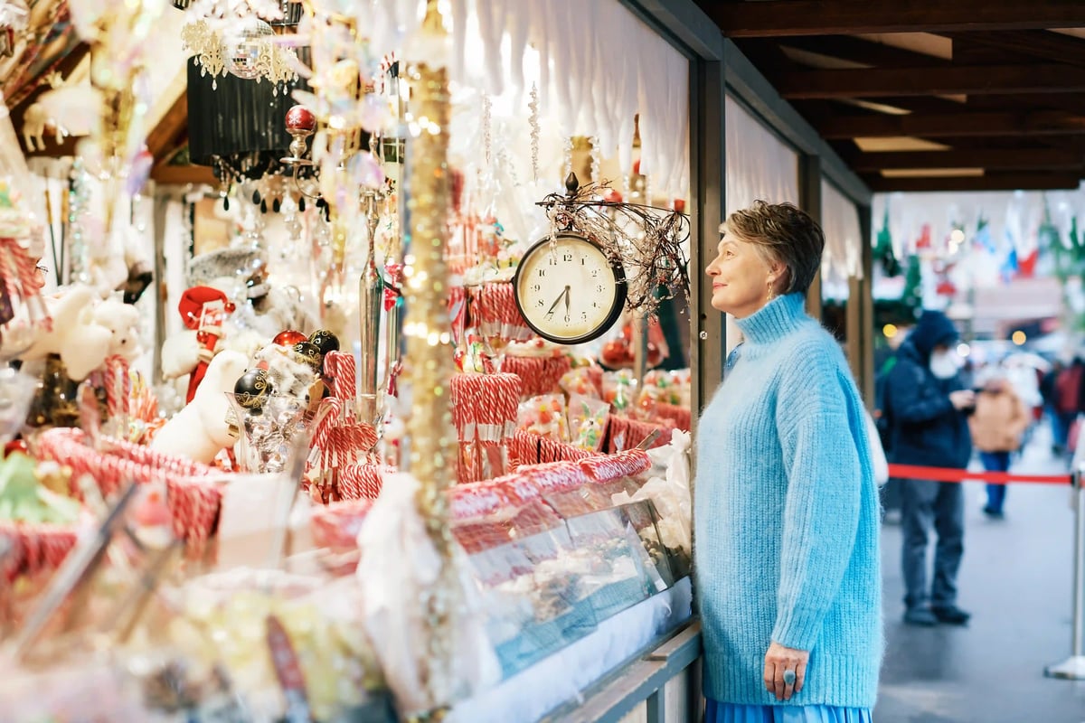 Frau betrachtet einen Stand auf einem Weihnachtsmarkt mit Dekoration und Suessigkeiten