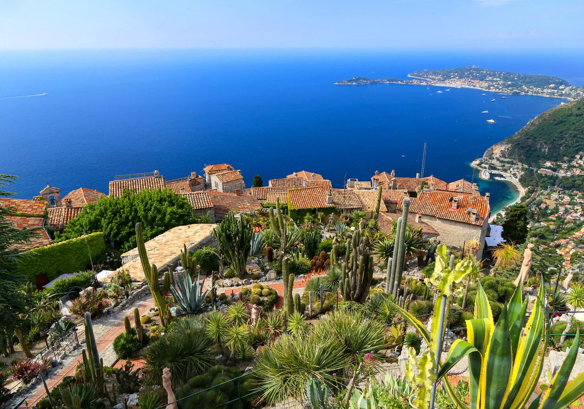 Vue sur des toits méditerranéens et des jardins luxuriants avec la mer bleu profond de la Côte d’Azur