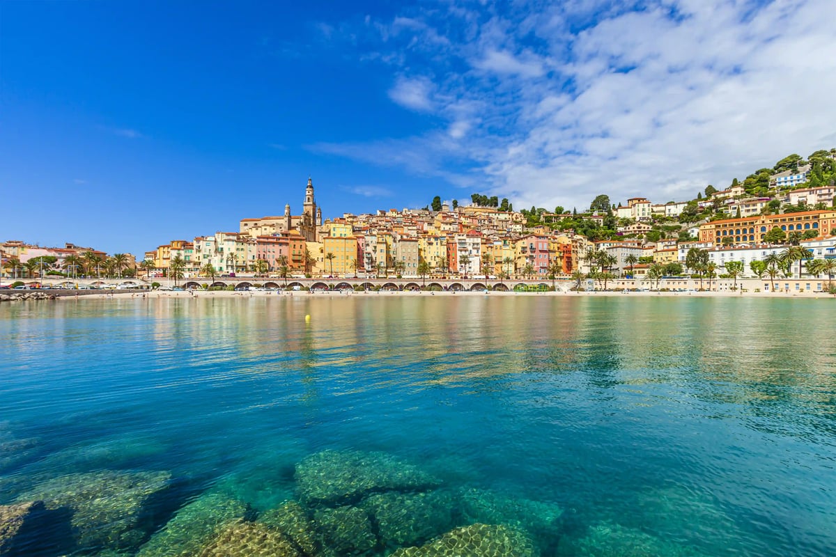 Vue sur la vieille ville colorée de Menton avec des palmiers, une promenade portuaire et une eau méditerranéenne claire