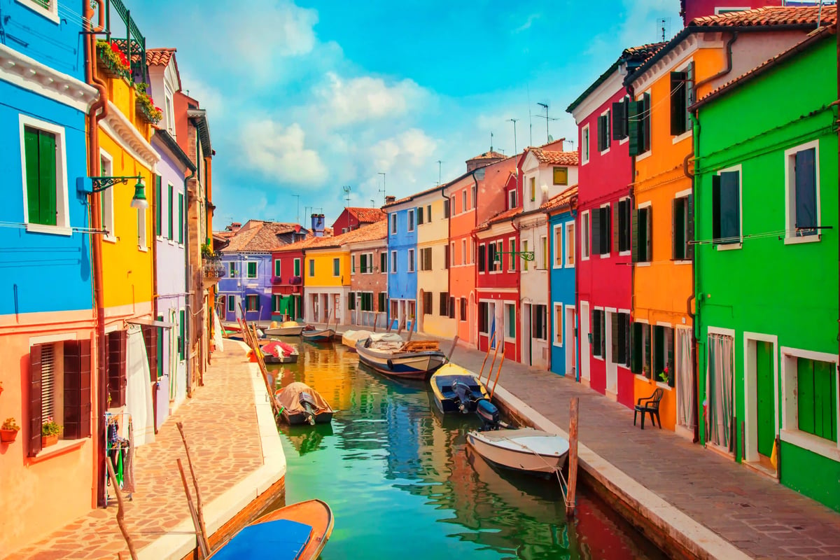 Canal coloré à Burano avec des façades vives et de petites barques amarrées le long des berges.