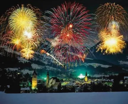 Buntes Feuerwerk über einem verschneiten Ort in den Alpen bei Nacht