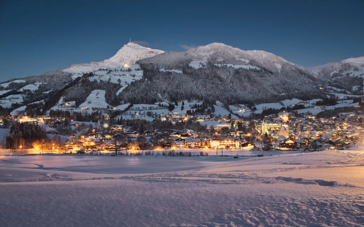 Winterliches Kitzbühel mit schneebedeckten Bergen und beleuchtetem Ortskern in der Abenddämmerung