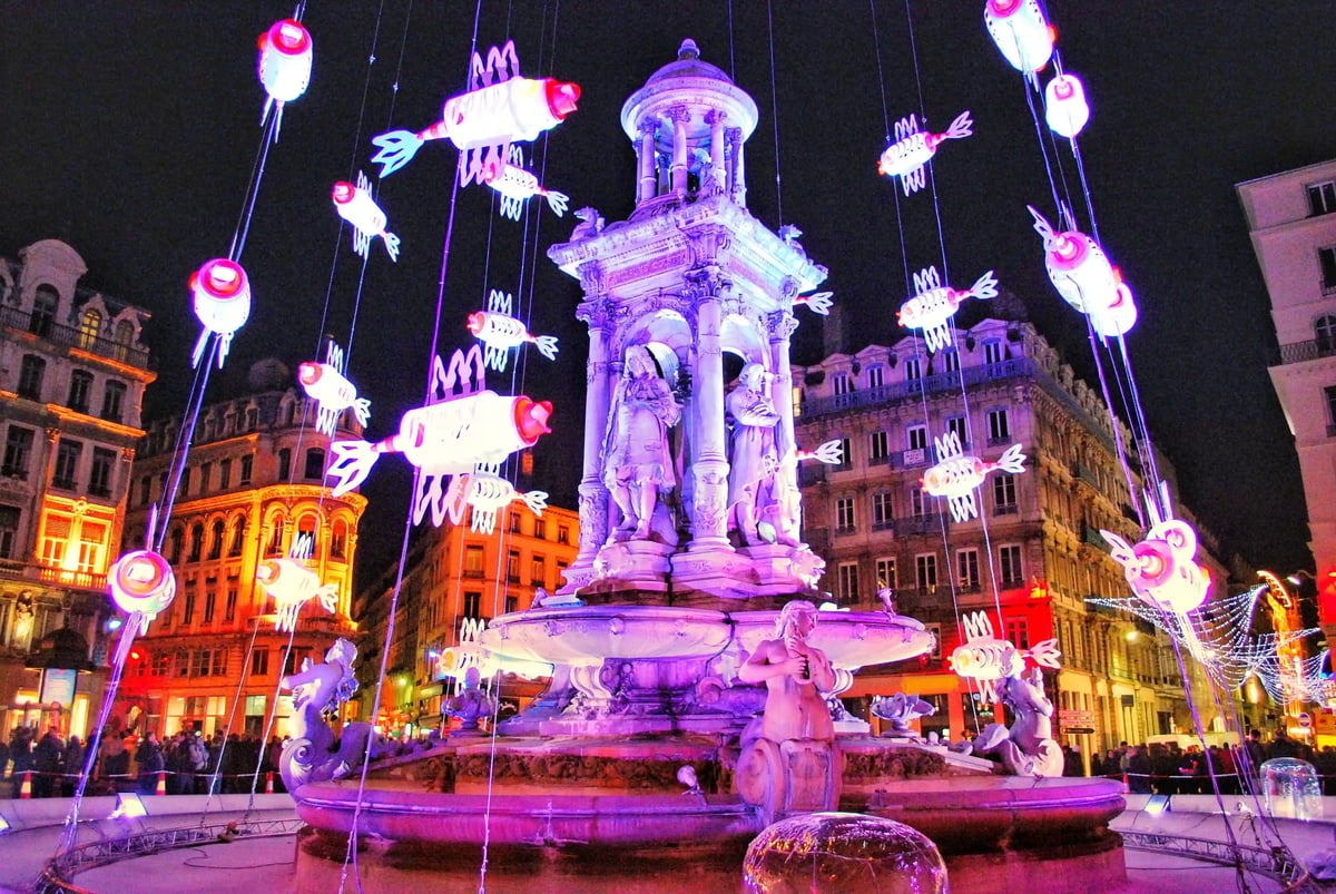 Kunstvolle Lichtinstallation mit leuchtenden Figuren rund um den Bartholdi-Brunnen während des Lichterfests in Lyon.