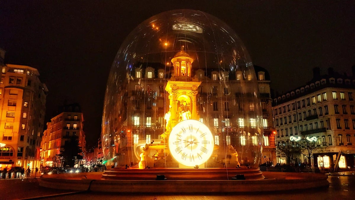 Fontaine illuminée de la place des Jacobins avec une grande horloge sous une coupole transparente.