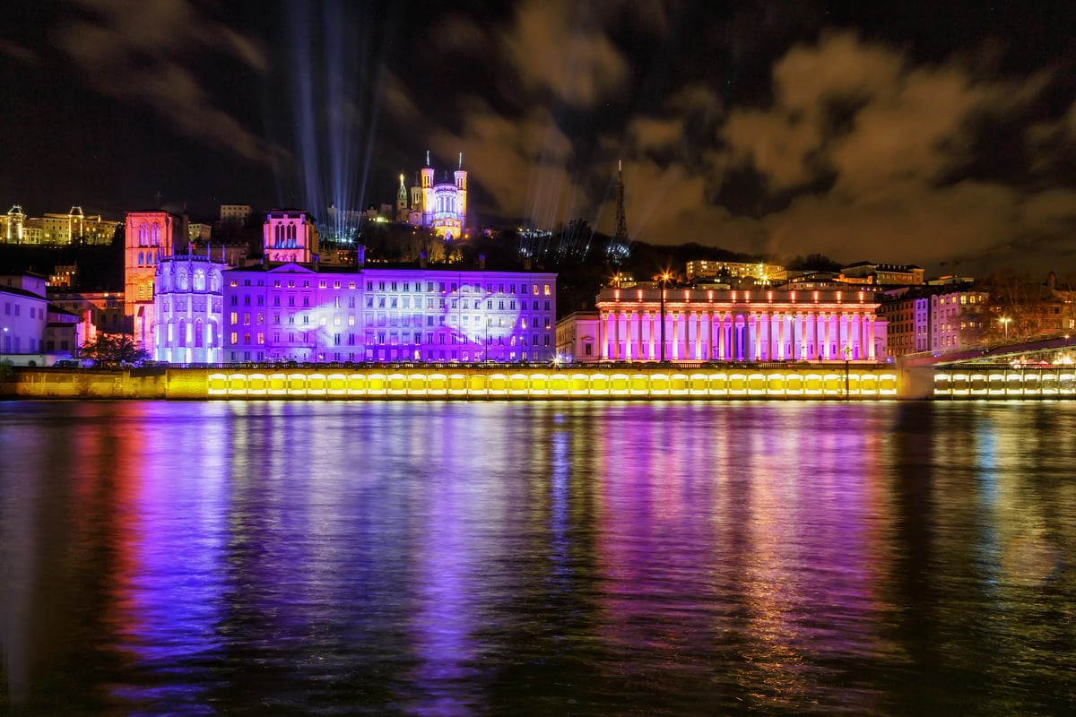 Quais de Saône illuminés avec bâtiments historiques et basilique Notre-Dame de Fourvière à Lyon.