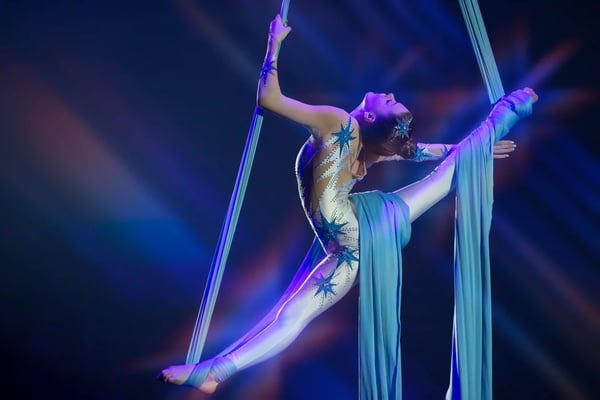 Artistin in einem Kostüm hängt an Lufttüchern während einer Zirkusvorstellung mit farbigem Licht