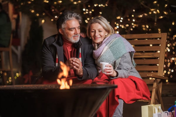 Paar sitzt am Feuer und trinkt heisse Getränke bei Nacht