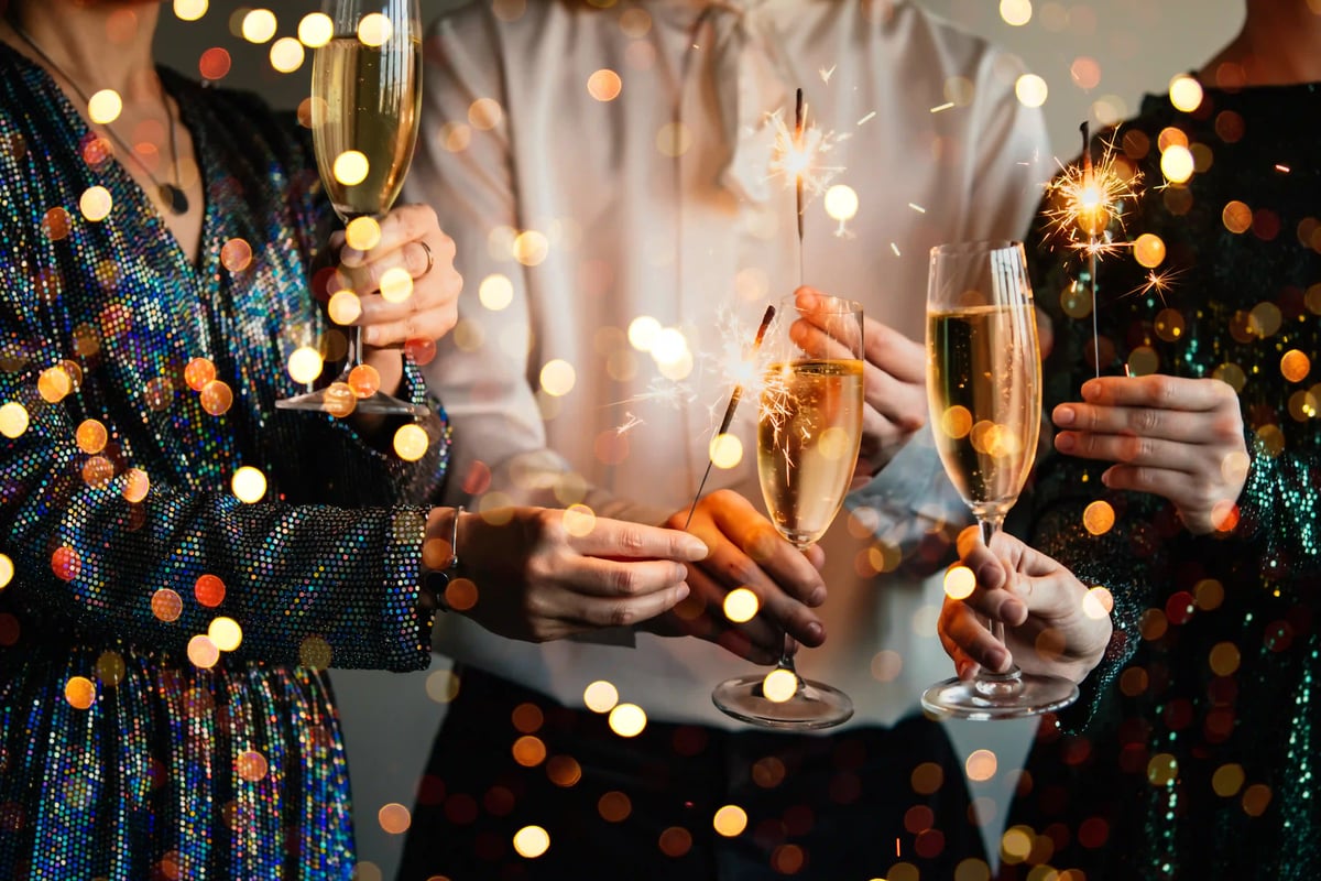 Personen mit Sektgläsern und Wunderkerzen feiern gemeinsam Silvester