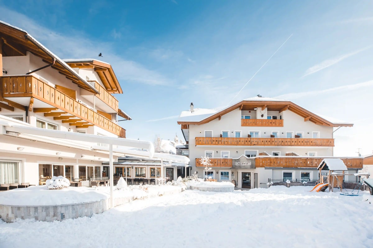 Verschneites Ferienhotel Oberwirt in Feldthurns mit Holzbalkonen unter blauem Winterhimmel