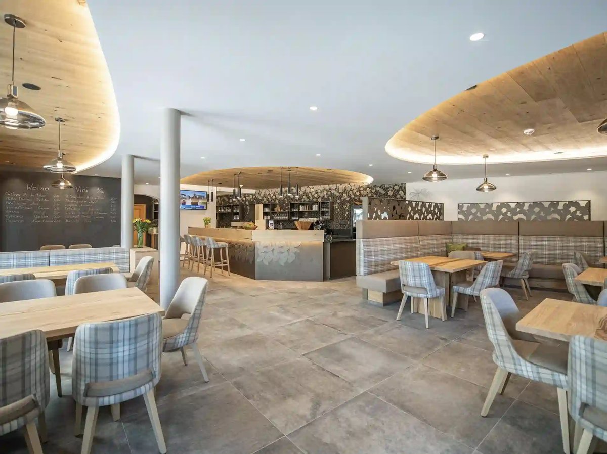 Modernes Hotelrestaurant mit Holztischen, gepolsterten Sitzbänken und zentraler Bar