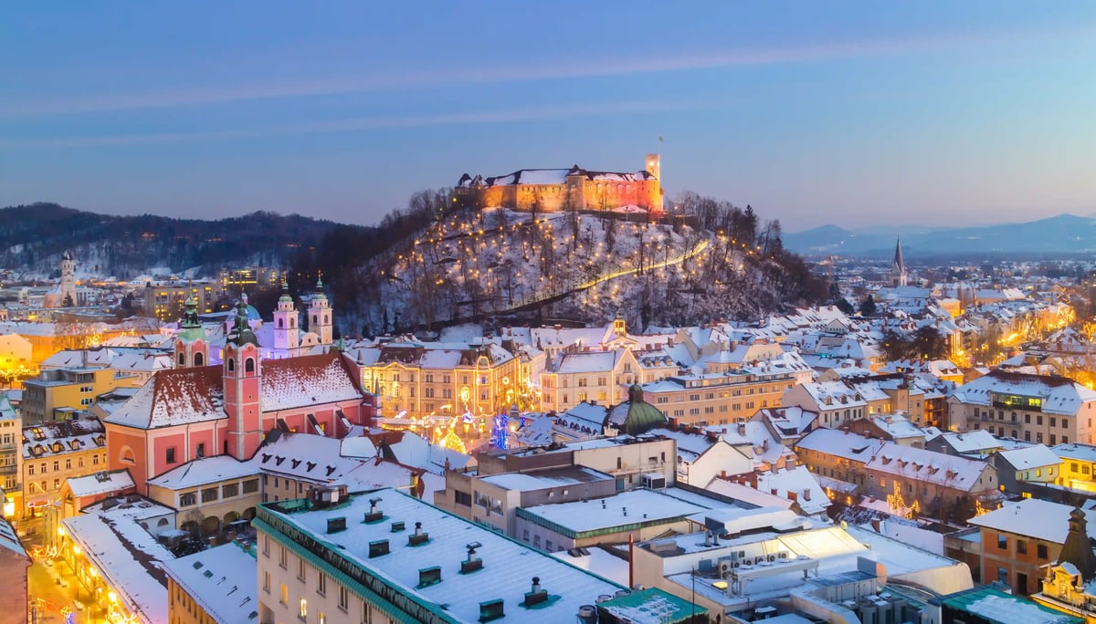 Winterliches Ljubljana mit Burg auf dem Schlossberg und verschneiter Altstadt in der Abenddämmerung.