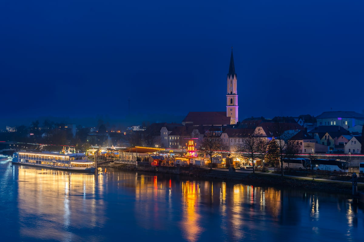 Abendstimmung an der Donau in Passau mit beleuchtetem Flussufer, Kirche und Flusskreuzfahrtschiff.
