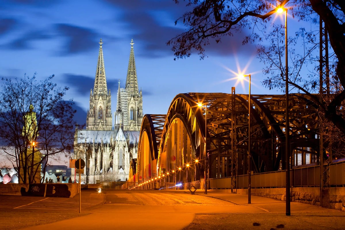  Vue sur la cathédrale de Cologne illuminée au crépuscule avec le pont Hohenzollern au premier plan.