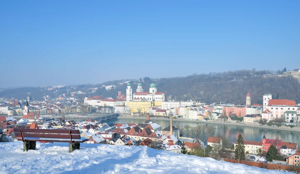 Winterlicher Blick über Passau mit schneebedeckten Dächern, Flusslandschaft und Dom St. Stephan im Hintergrund