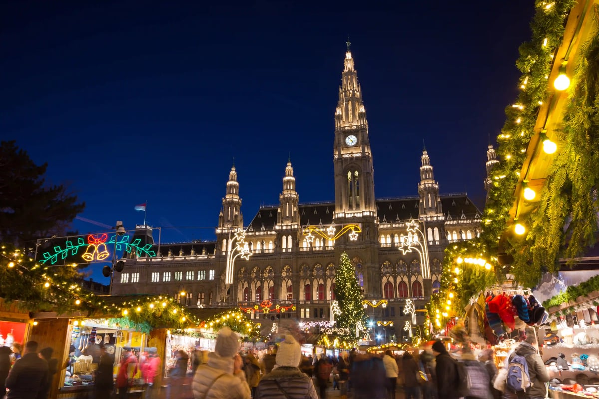 Wiener Rathausplatz bei Nacht mit Weihnachtsbeleuchtung und belebtem Marktgeschehen