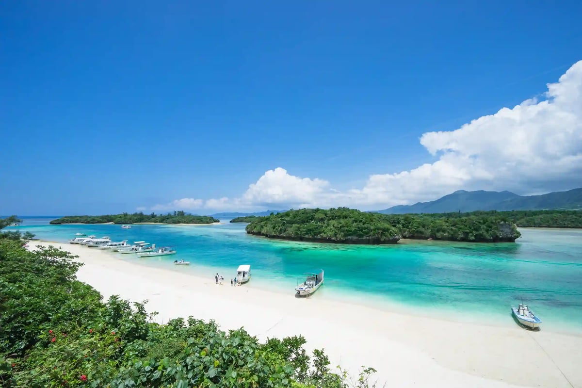Sandstrand mit türkisem Meer, kleinen Booten und bewaldeten Inseln