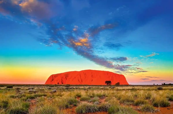 Roter Felsen Uluru im australischen Outback bei Sonnenuntergang unter farbigem Himmel