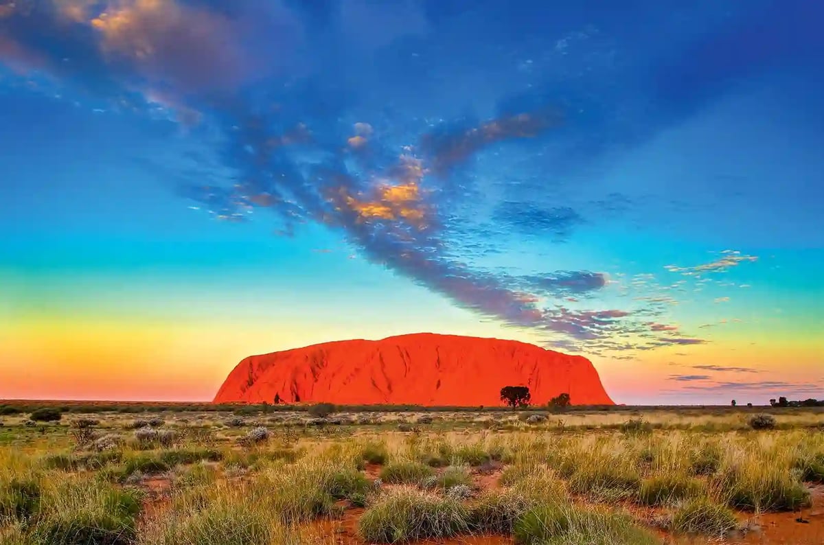 Roter Felsen Uluru im australischen Outback bei Sonnenuntergang unter farbigem Himmel