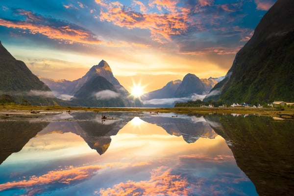 Dramatische Berglandschaft im Fiordland Nationalpark mit Sonnenaufgang und Spiegelung im ruhigen Wasser