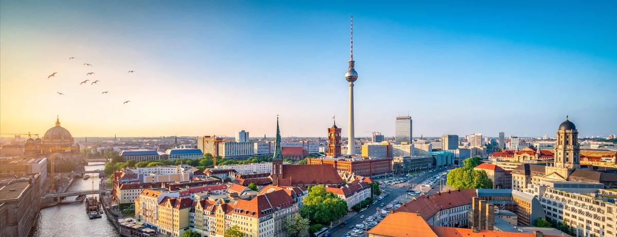 Panorama von Berlin bei Sonnenuntergang mit Fernsehturm, Spree und Dächermeer der Innenstadt.