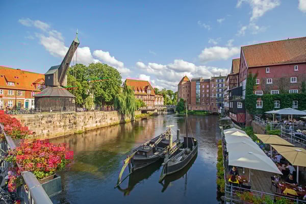 Farbige Fachwerkhäuser an einem Kanal in Lüneburg, belebte Uferterrassen und Blumen am Brueckengeländer