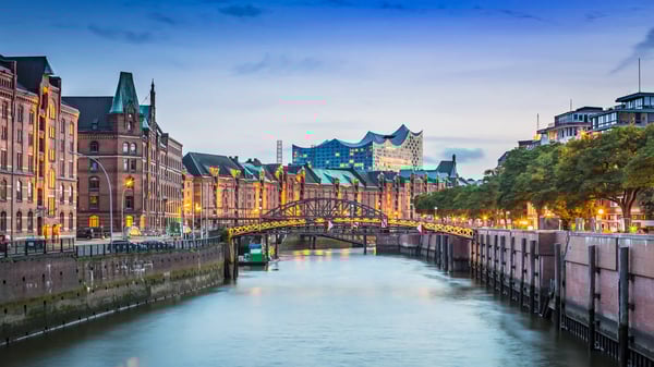 Blick durch einen Fleet in Hamburgs Speicherstadt mit beleuchteter Brücke und Backsteinspeichern, dahinter die Elbphilharmonie in der Abenddämmerung.