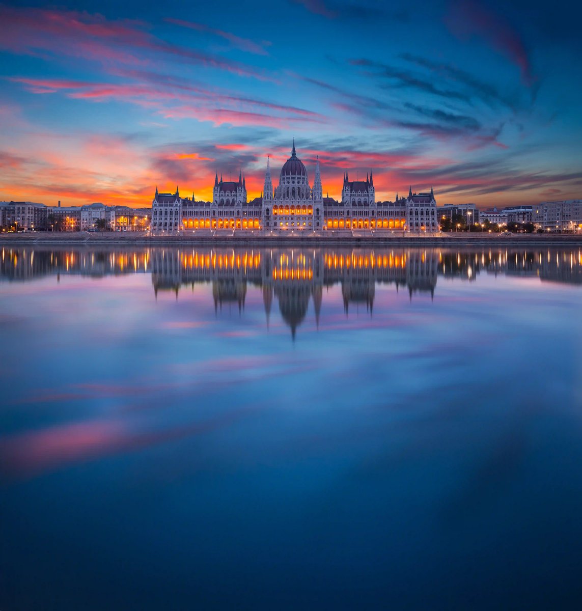 Bâtiment du Parlement hongrois à Budapest au coucher du soleil avec reflet dans les eaux calmes du Danube