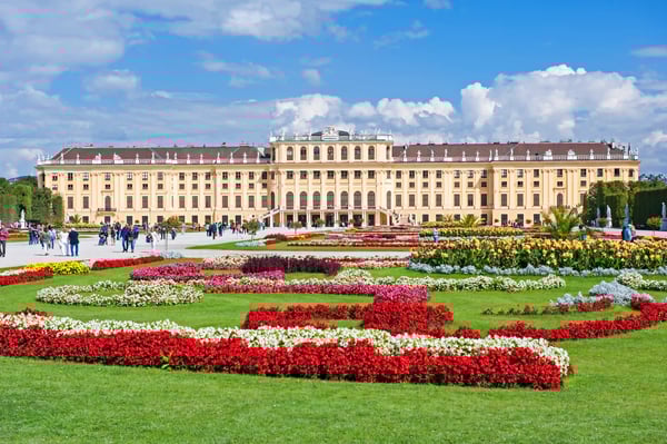 Schloss Schönbrunn in Wien mit barocker Fassade und grosszügigem Garten mit bunten Blumenbeeten im Vordergrund